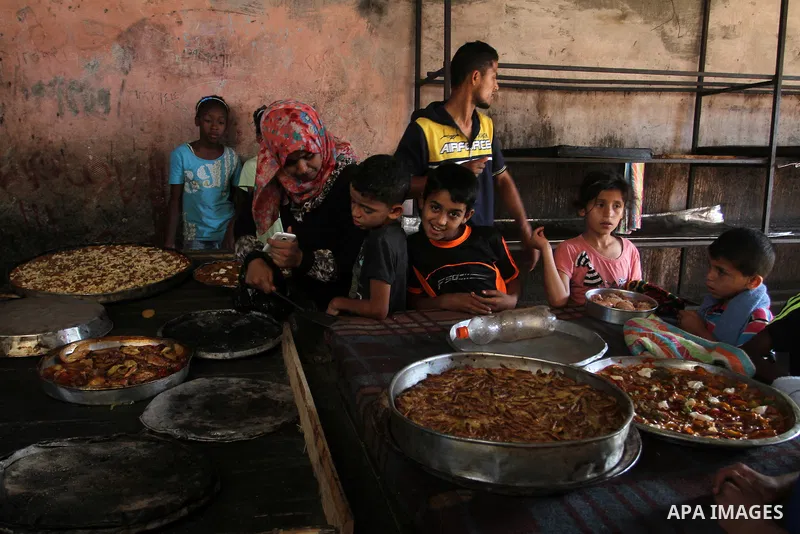 Palestinians wait as they cook their foods in a traditional mud oven during the holy fasting month of Ramadan, in Rafah in the southern Gaza Strip on June 19, 2016. Ramadan is sacred to Muslims because it is during that...