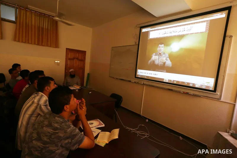 A Palestinian imam sits next to a screen with a projection of a man reading the Koran, Islam's holy book, with sign-language during a class at a religion school in Gaza City on June 21, 2016, during the Muslim fasting mo...