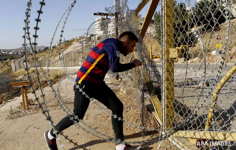 A Palestinian passes through an opening in the Israeli barrier fence as he attempts to make his way to attend the third Friday prayer of the holy fasting month of Ramadan in Jerusalem's al-Aqsa mosque, near the West bank...