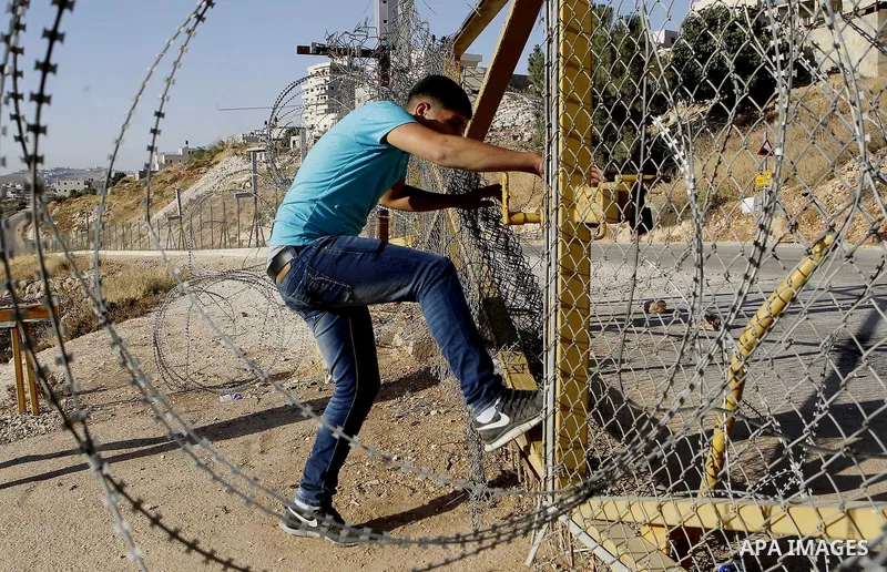 A Palestinian passes through an opening in the Israeli barrier fence as he attempts to make his way to attend the third Friday prayer of the holy fasting month of Ramadan in Jerusalem's al-Aqsa mosque, near the West bank...