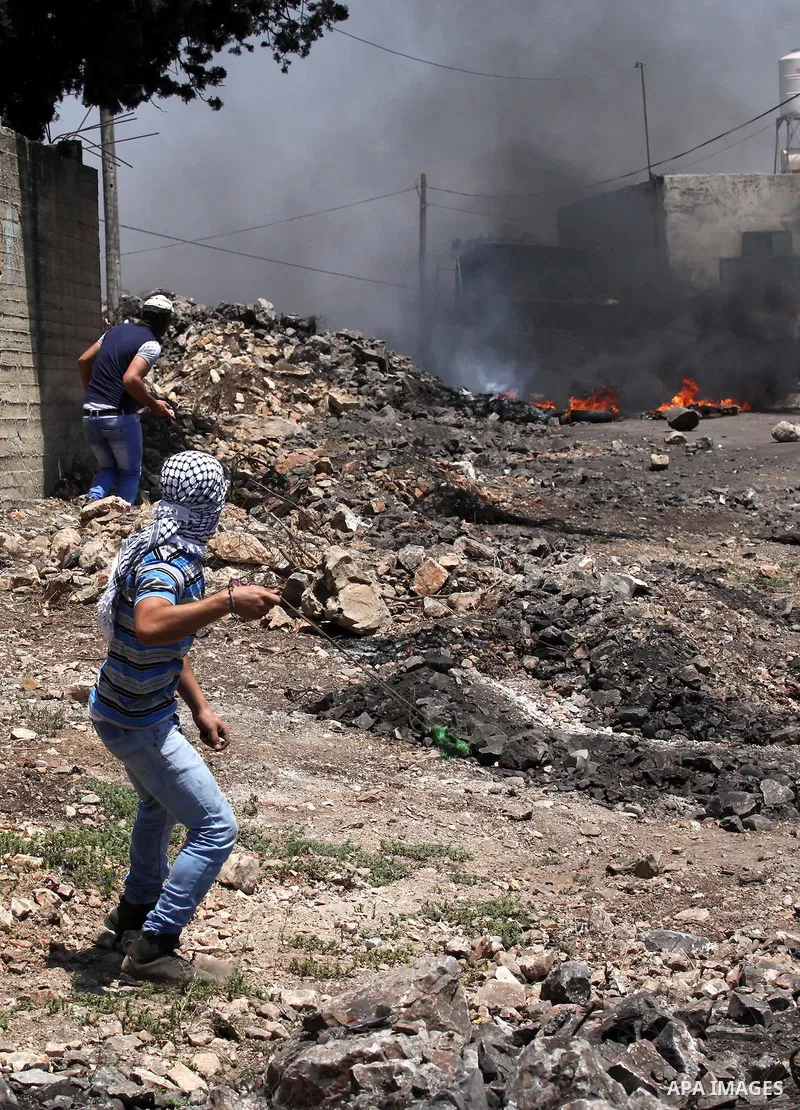 A Palestinian protester uses a slingshot to hurl stones towards Israeli security forces during clashes following a demonstration against the expropriation of Palestinian land by Israel on June 24, 2016 in the village of...