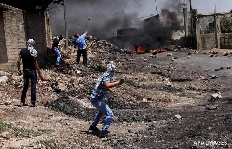 Palestinian protesters use a slingshot to hurl stones towards Israeli security forces during clashes following a demonstration against the expropriation of Palestinian land by Israel on June 24, 2016 in the village of Kf...