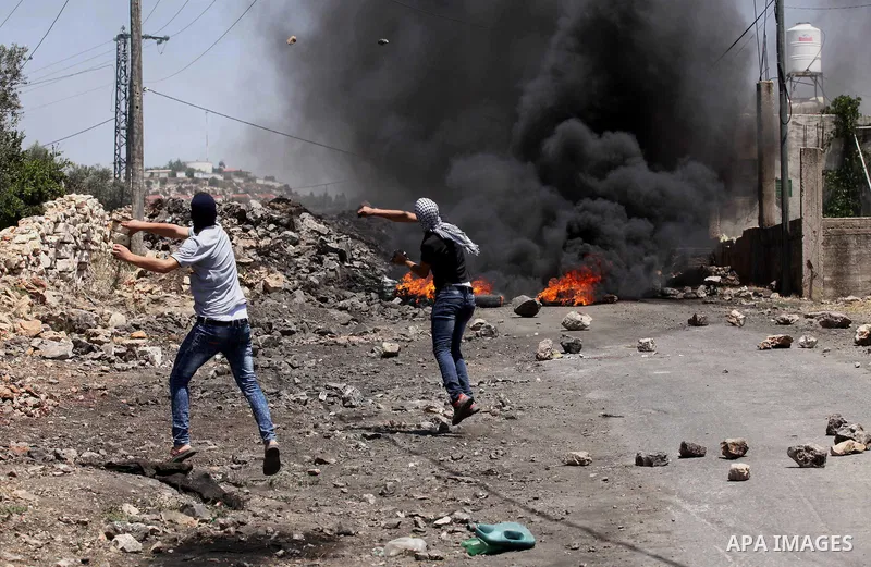 Palestinian protesters use a slingshot to hurl stones towards Israeli security forces during clashes following a demonstration against the expropriation of Palestinian land by Israel on June 24, 2016 in the village of Kf...