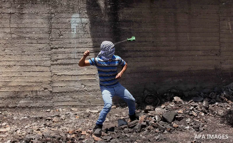 A Palestinian protester uses a slingshot to hurl stones towards Israeli security forces during clashes following a demonstration against the expropriation of Palestinian land by Israel on June 24, 2016 in the village of...