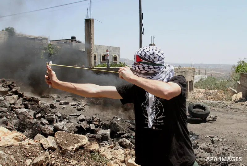 A Palestinian protester uses a slingshot to hurl stones towards Israeli security forces during clashes following a demonstration against the expropriation of Palestinian land by Israel on June 24, 2016 in the village of...