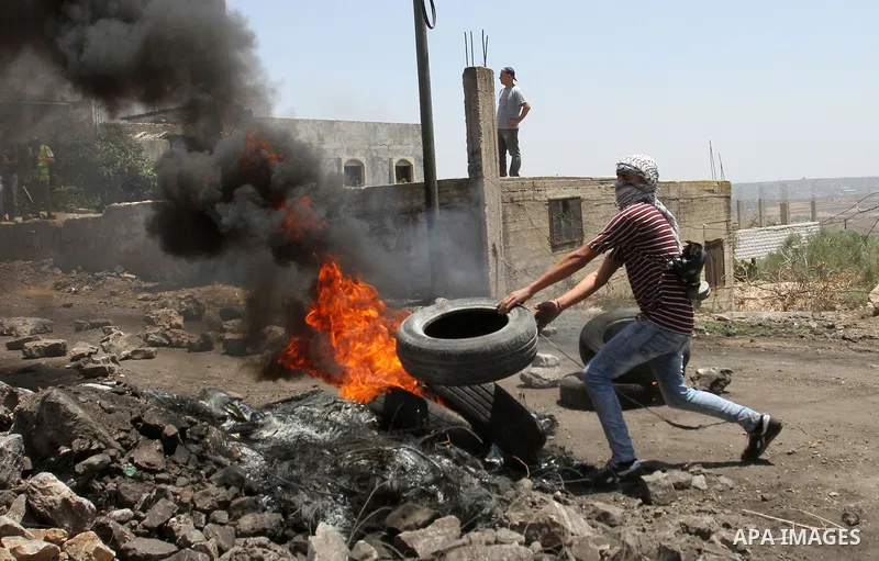 A Palestinian protester burns tires during clashes with Israeli security forces during clashes following a demonstration against the expropriation of Palestinian land by Israel on June 24, 2016 in the village of Kfar Qad...