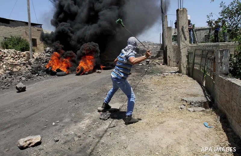 A Palestinian protester uses a slingshot to hurl stones towards Israeli security forces during clashes following a demonstration against the expropriation of Palestinian land by Israel on June 24, 2016 in the village of...