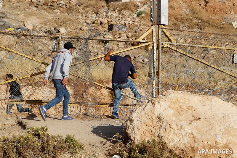 Palestinian men cross through a gap in the barbed-wire gate part of the controversial Israeli separation fence between the West Bank town of Bethlehem and Jerusalem, in an attempt to reach the Al-Aqsa Mosque compound in...