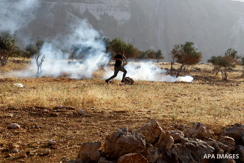 Palestinians run for a cover from teargas canisters fired by Israeli border police near a barbed-wire gate part of the controversial Israeli separation fence between the West Bank town of Bethlehem and Jerusalem, after a...
