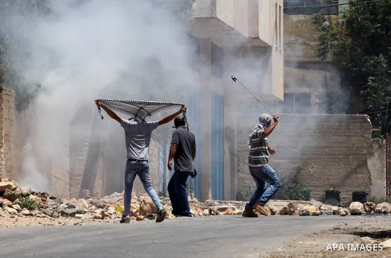 A Palestinian protester uses a slingshot to hurl stones towards Israeli security forces during clashes following a demonstration against the expropriation of Palestinian land by Israel on July 01, 2016 in the village of...