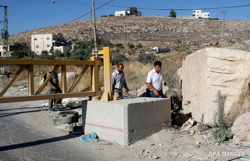 Palestinians walk past a barrier blocking the road in the village of Halhul north of the Israeli occupied West Bank city of Hebron, July 2, 2016. The entire city of Hebron was placed under a general closure, while transf...