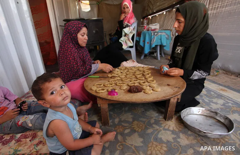 A Palestinian family, whose house was destroeyed during 2014 war, make traditional cakes inside their makeshift shelter, ahead of Eid-al-Fitr celebrations in Khan Younis in the southern Gaza Strip July 3, 2016. Photo by...