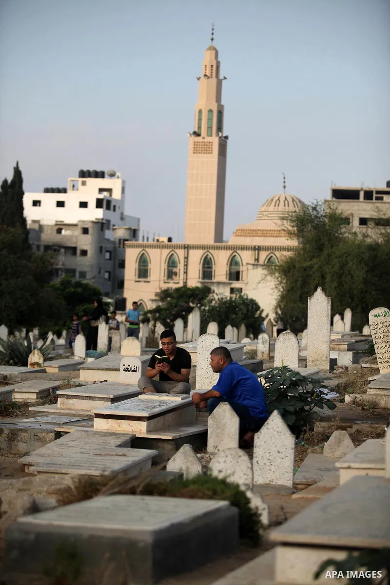 Palestinian men read the Koran next to the grave of their relative at a cemetery on the first day of Eid al-Fitr celebrations, which marks the end of the holy fasting month of Ramadan, in Gaza City July 6, 2016. Photo by...