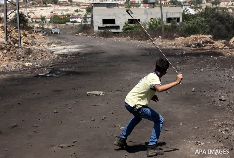 A Palestinian protester uses a slingshot to hurl stones towards Israeli security forces during clashes following a demonstration against the expropriation of Palestinian land by Israel on July 08, 2016 in the village of...