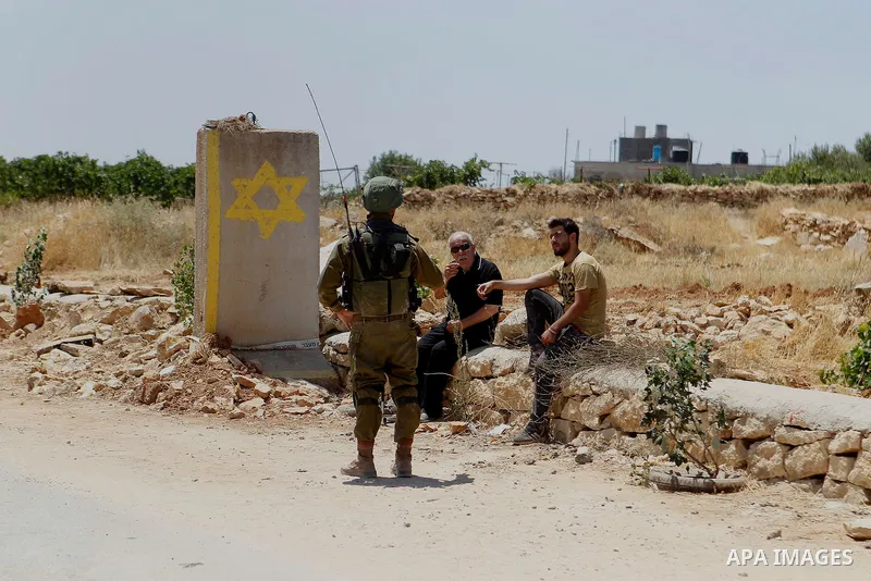 A Palestinian man speaks with a member of Israeli security forces as he wait to cross at an entrance of the West Bank village of Sair, east of Hebron, on July 11, 2016 as the Israeli army keeps the area under lockdown af...