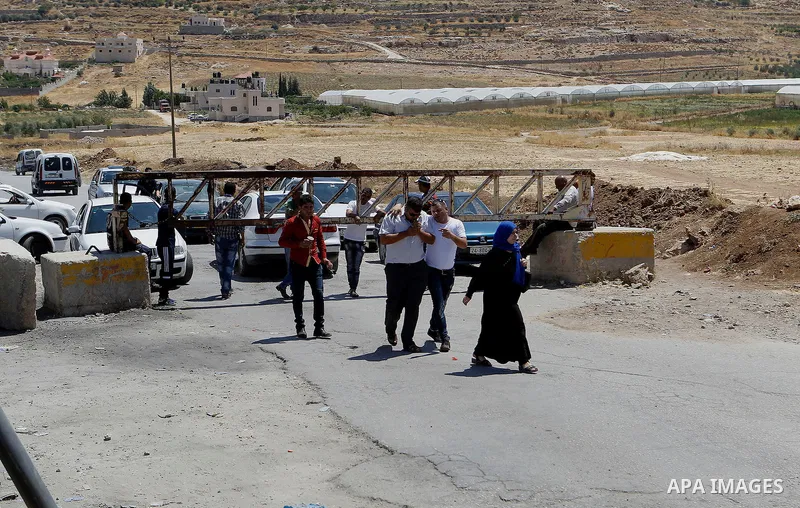 Drivers wait in front of a closed gate while pedestrians cross at an entrance of the West Bank of Al-Fawwar refugee camp, south of Hebron on July 11, 2016 as the Israeli army keeps the area under lockdown afer an Israeli...