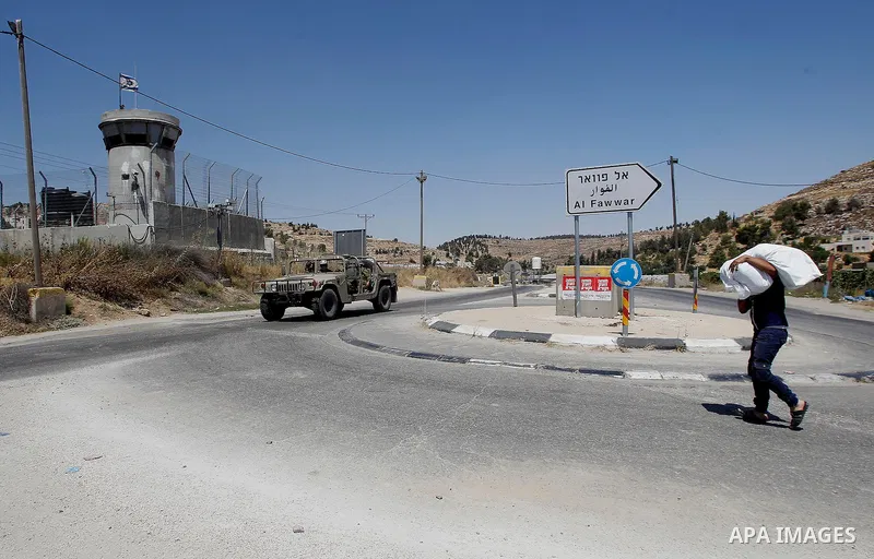 Drivers wait in front of a closed gate while pedestrians cross at an entrance of the West Bank of Al-Fawwar refugee camp, south of Hebron on July 11, 2016 as the Israeli army keeps the area under lockdown afer an Israeli...