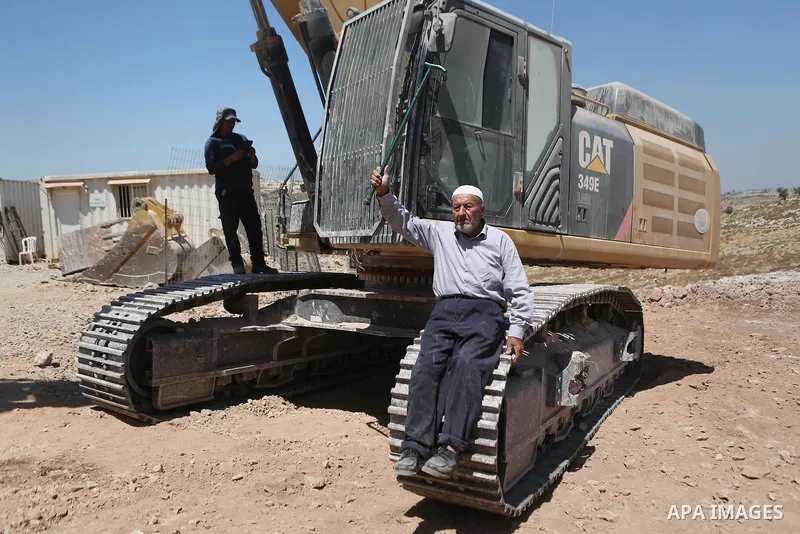 A Palestinian man sits on a tracks of an Israeli excavator as he tries to prevent it from clearing his land during a protest against Jewish settlements, near the village of Deir Qaddis near the West Bank city of Ramallah...