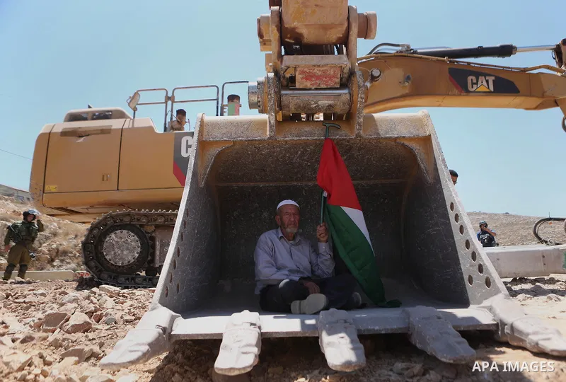 A man holding a Palestinian flag protests as he sits in the scoop of an Israeli excavator as tries to prevent it from clearing his land during a protest against Jewish settlements, near the village of Deir Qaddis near th...