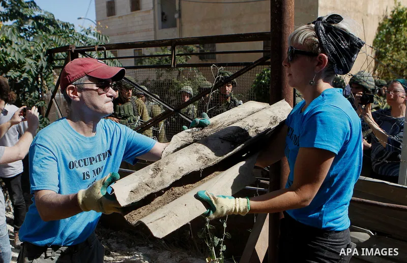 Peace activists clean around Palestinian houses as Israeli army soldiers stand guard in Tal Rumaida in the West Bank city of Hebron July 15, 2016. Photo by Wisam Hashlamoun
