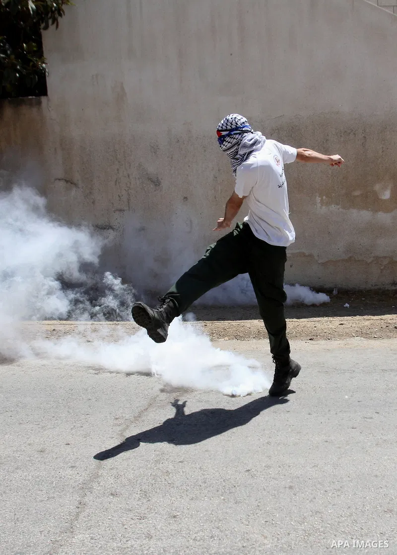 A Palestinian protester kicks back a tear gas canister fired by Israeli security forces during clashes following a demonstration against the expropriation of Palestinian land by Israel on July 15, 2016 in the village of...