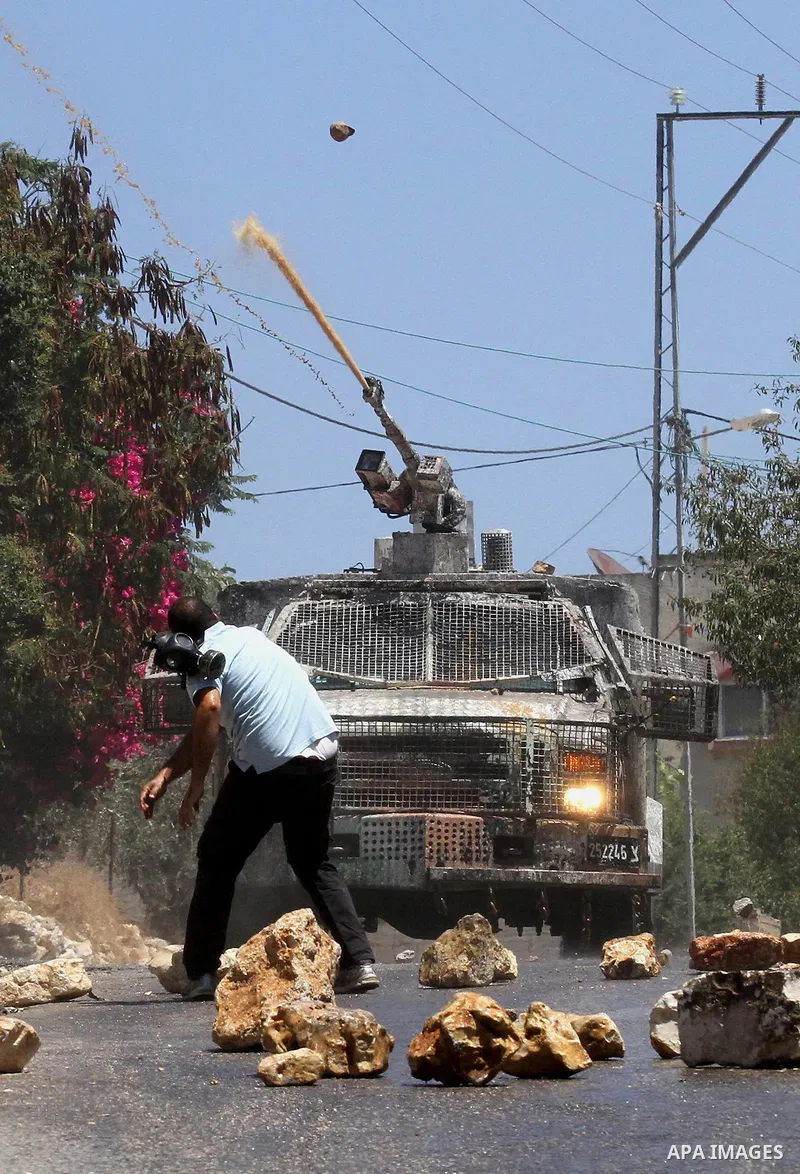 A Palestinian protester throws stones towards an Israeli security forces vehicle spraying a foul-smelling water known as "skunk" during clashes following the weekly demonstration against the expropriation of Palestinian...