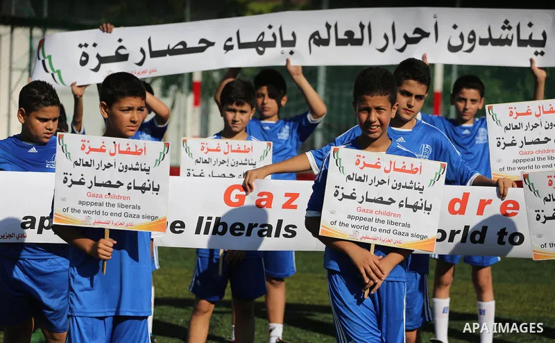 Palestinian boys hold placards demanding for end the siege during a training season for football school at Al Jazeera club in Gaza city, on July 26, 2016. Photo by Mohammed Asad