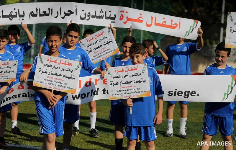 Palestinian boys hold placards demanding for end the siege during a training season for football school at Al Jazeera club in Gaza city, on July 26, 2016. Photo by Mohammed Asad