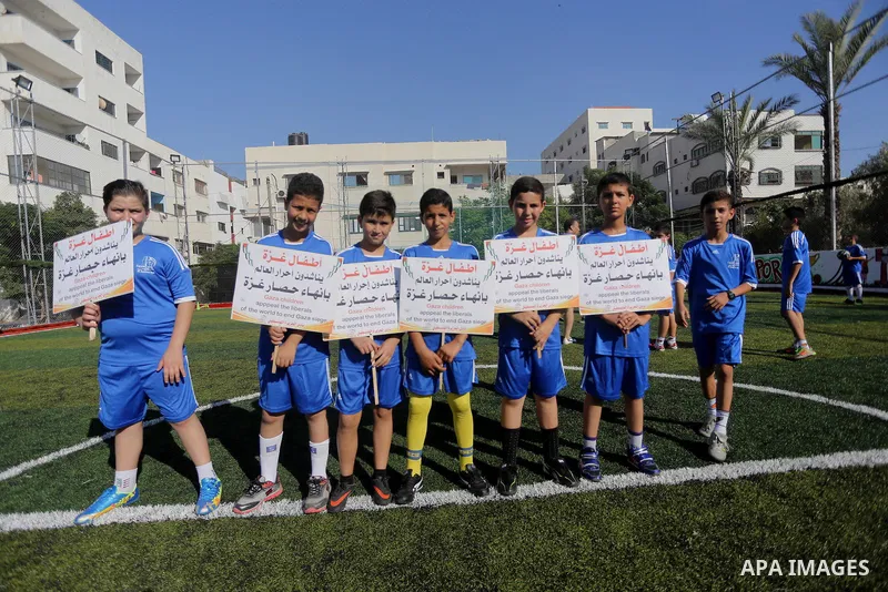 Palestinian boys hold placards demanding for end the siege during a training season for football school at Al Jazeera club in Gaza city, on July 26, 2016. Photo by Mohammed Asad