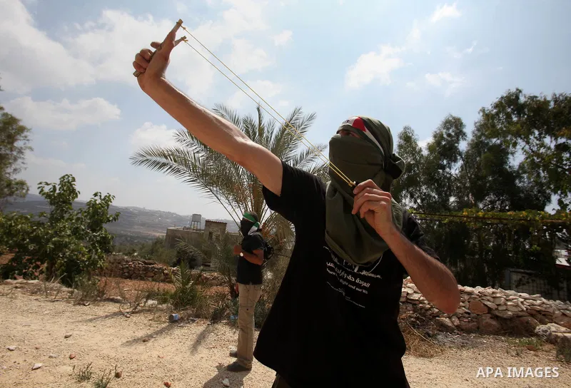 A Palestinian protestor uses a slingshot to hurl stones towards Israeli security forces during clashes following the weekly demonstration against the expropriation of Palestinian land by Israel in the village of Kfar Qad...