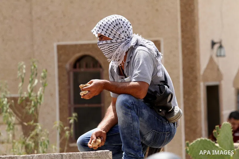 A Palestinian protestor squats on top of a wall holding stones during clashes with Israeli security forces following the weekly demonstration against the expropriation of Palestinian land by Israel in the village of Kfar...