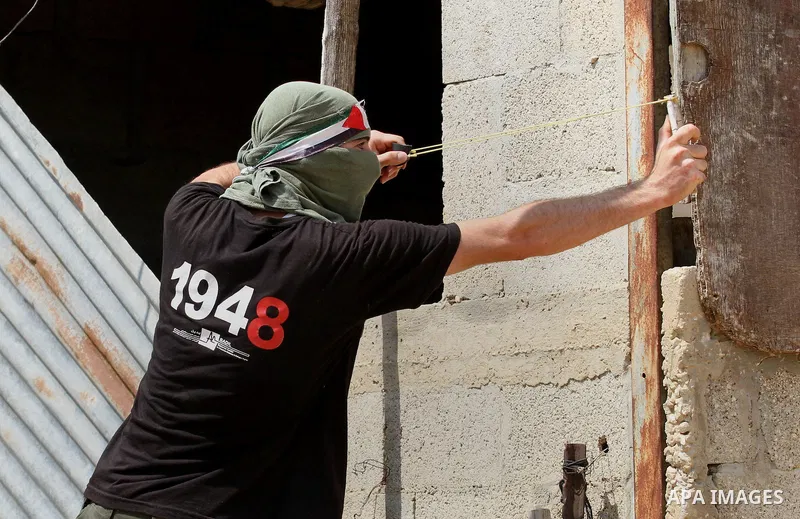 A Palestinian protestor uses a slingshot to hurl stones towards Israeli security forces during clashes following the weekly demonstration against the expropriation of Palestinian land by Israel in the village of Kfar Qad...