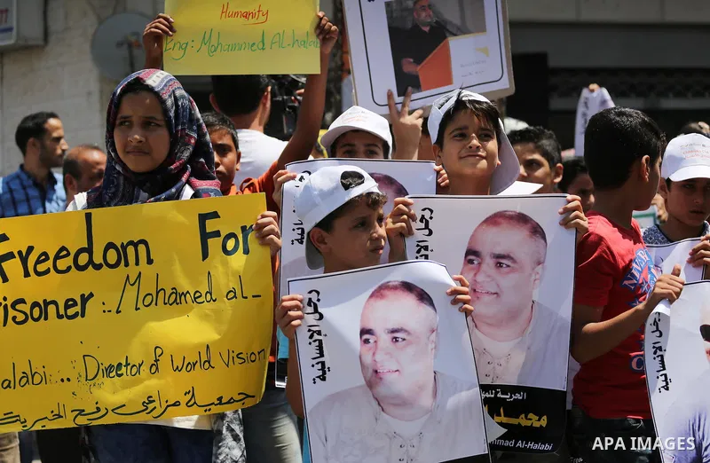 Palestinian demonstrators hold posters of Mohammad El Halabi, World Vision's manager of operations in Gaza who was accused by Israel of funnelling millions of dollars in aid money to Hamas, during a protest in solidarity...