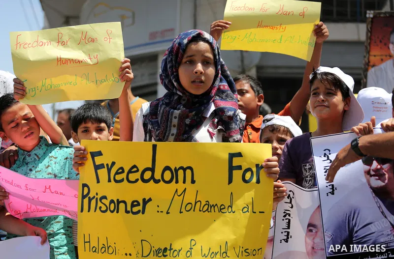 Palestinian demonstrators hold posters of Mohammad El Halabi, World Vision's manager of operations in Gaza who was accused by Israel of funnelling millions of dollars in aid money to Hamas, during a protest in solidarity...
