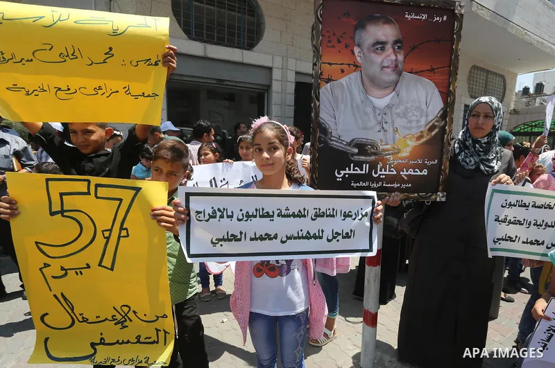 Palestinian demonstrators hold posters of Mohammad El Halabi, World Vision's manager of operations in Gaza who was accused by Israel of funnelling millions of dollars in aid money to Hamas, during a protest in solidarity...