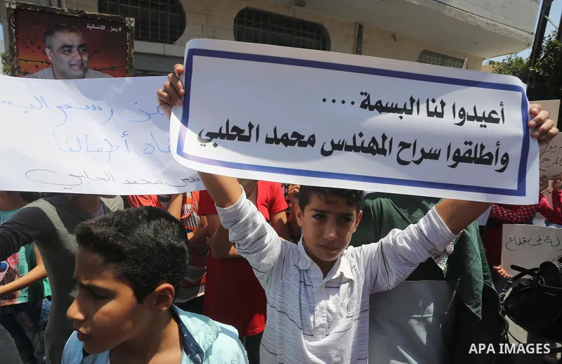 Palestinian demonstrators hold posters of Mohammad El Halabi, World Vision's manager of operations in Gaza who was accused by Israel of funnelling millions of dollars in aid money to Hamas, during a protest in solidarity...