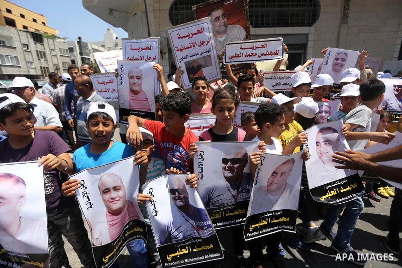 Palestinian demonstrators hold posters of Mohammad El Halabi, World Vision's manager of operations in Gaza who was accused by Israel of funnelling millions of dollars in aid money to Hamas, during a protest in solidarity...