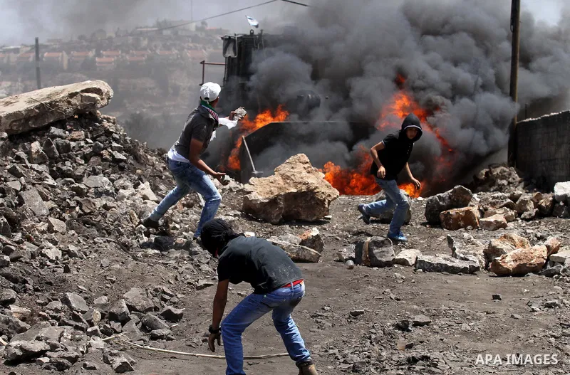 Palestinian protesters hurl stones toward an Israeli military bulldozer during clashes with Israeli security forces following a weekly demonstration against the expropriation of Palestinian land by Israel on August 12, 2...
