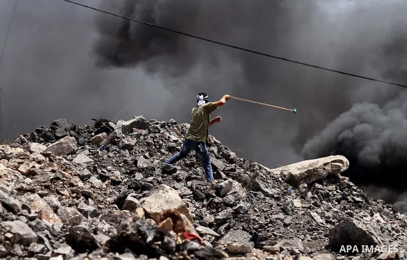 A Palestinian protester uses a slingshot to hurl stones toward Israeli security forces during clashes following a weekly demonstration against the expropriation of Palestinian land by Israel on August 12, 2016, in the vi...