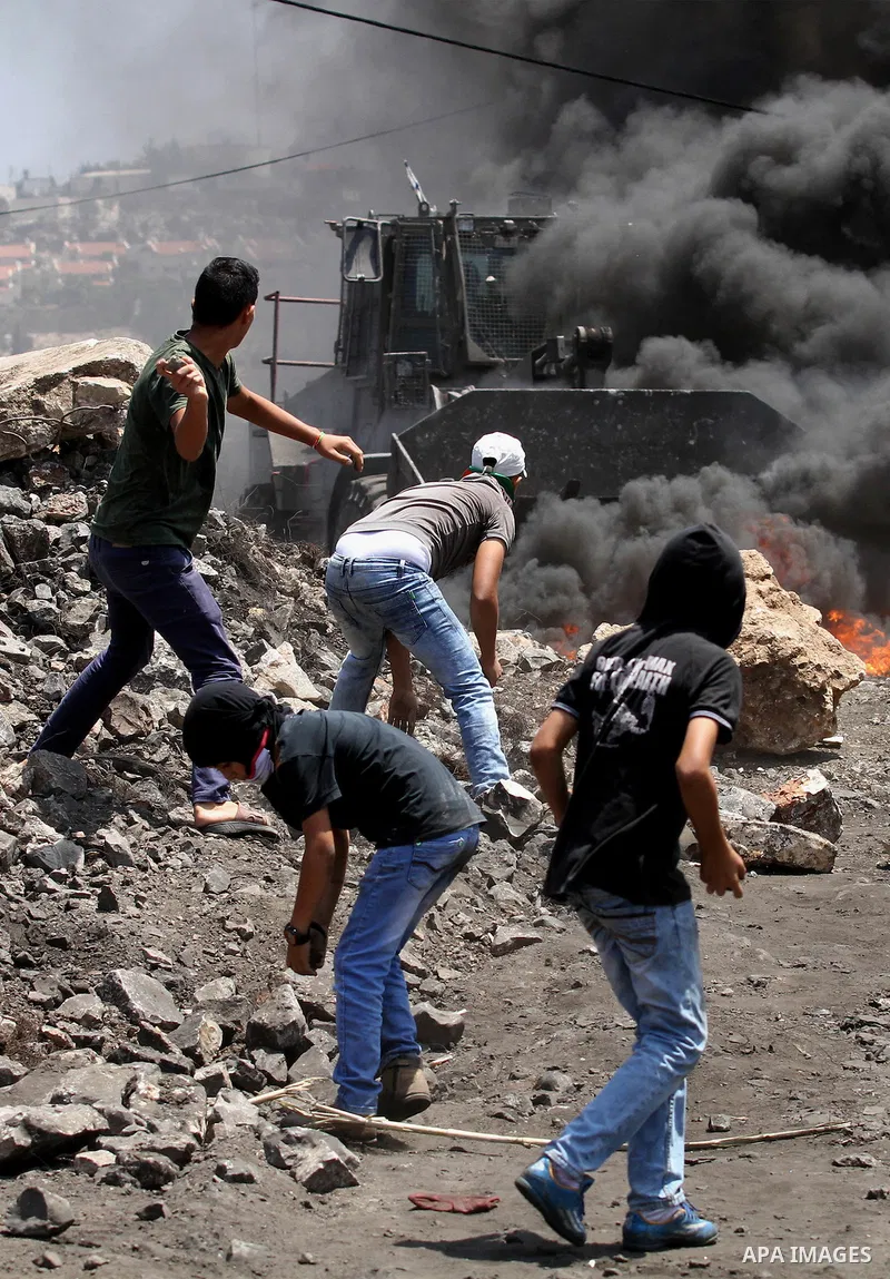 Palestinian protesters hurl stones toward an Israeli military bulldozer during clashes with Israeli security forces following a weekly demonstration against the expropriation of Palestinian land by Israel on August 12, 2...