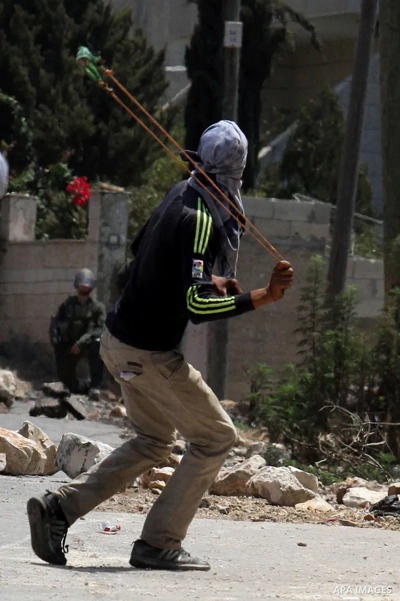 A Palestinian protester uses a slingshot to hurl stones toward Israeli security forces during clashes following a weekly demonstration against the expropriation of Palestinian land by Israel on August 12, 2016, in the vi...