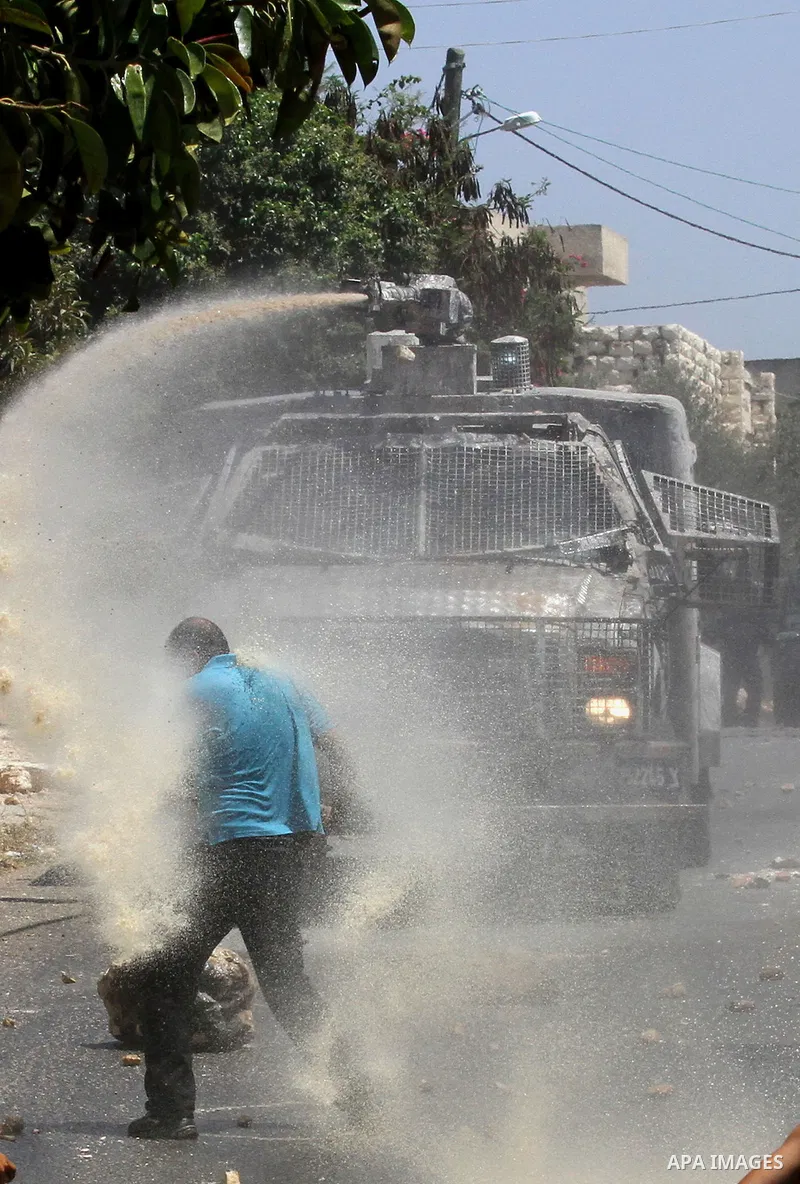 A Palestinian protester hurls stones towards an Israeli security forces vehicle spraying a foul-smelling water known as "skunk" during clashes following a weekly demonstration against the expropriation of Palestinian lan...