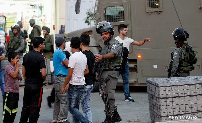 Israeli soldiers stand guard as Israeli settlers walk on a street in a Palestinian neighbourhood in the divided West Bank city of Hebron as they are heading to the Jewish shrine of Atnaeil Ben Kinaz on August 14,2016. Or...