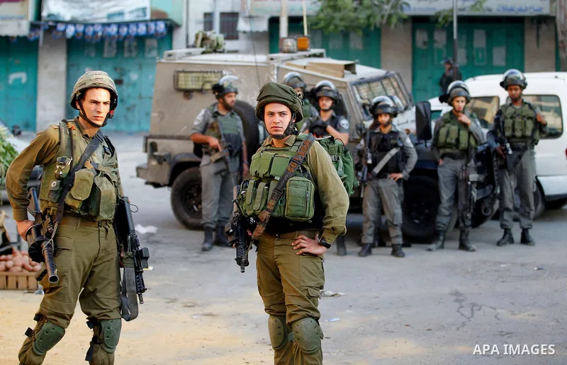 Israeli soldiers stand guard as Israeli settlers walk on a street in a Palestinian neighbourhood in the divided West Bank city of Hebron as they are heading to the Jewish shrine of Atnaeil Ben Kinaz on August 14,2016. Or...