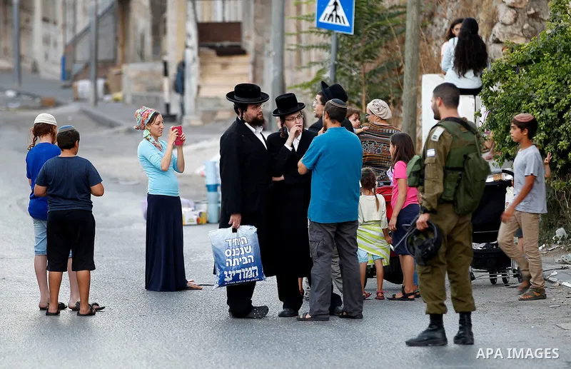 An Israeli soldier stands guard as Israeli settlers walk on a street in a Palestinian neighbourhood in the divided West Bank city of Hebron as they are heading to the Jewish shrine of Atnaeil Ben Kinaz on August 14,2016....