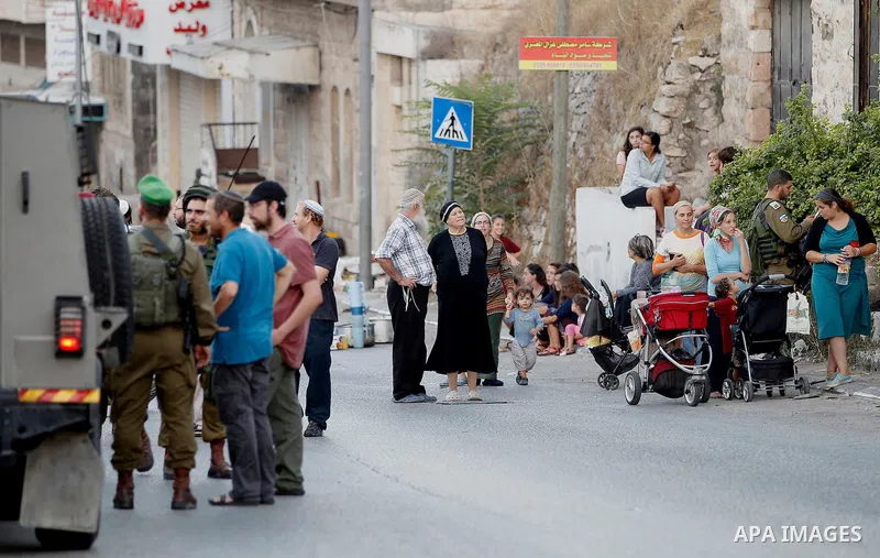 Israeli soldiers stand guard as Israeli settlers walk on a street in a Palestinian neighbourhood in the divided West Bank city of Hebron as they are heading to the Jewish shrine of Atnaeil Ben Kinaz on August 14,2016. Or...