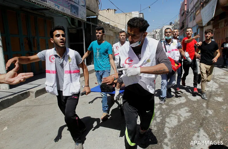 Members of the Palestinian Red Crescent and medics evacuate on a stretcher a Palestinian youth who was wounded during clashes with Israeli soldiers conducting searches in the Palestinian al-Fawwar refugee camp, south of...