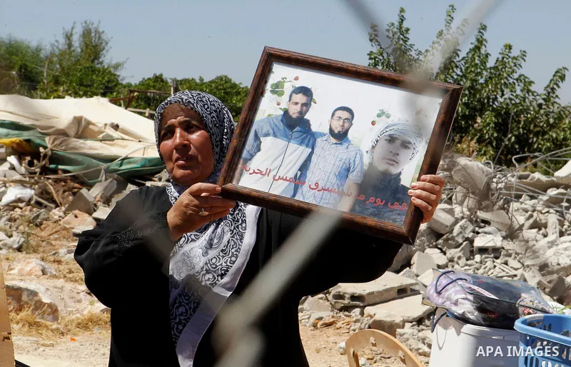 A Palestinian woman gestures as she holds a picture of her sons, two of whom are held in Israeli jails, after Israeli troops demolished her house in the West Bank village of Saeer, near Hebron August 16, 2016. Photo by W...
