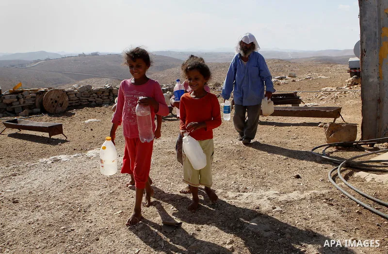 Palestinians carry plastic bottles and jerry cans filled with drinking water from a water tank in the West Bank village of Um Alkhair south of Hebron on August 17, 2016. Photo by Wisam Hashlamoun