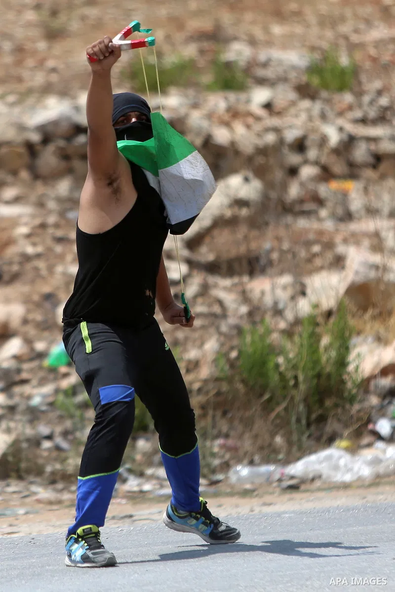 A Palestinian protester uses a slingshot to hurl stones towards Israeli troops during clashes following a protest in solidarity with Palestinian prisoners held in Israeli jails, near Israel's Ofer Prison near the West Ba...
